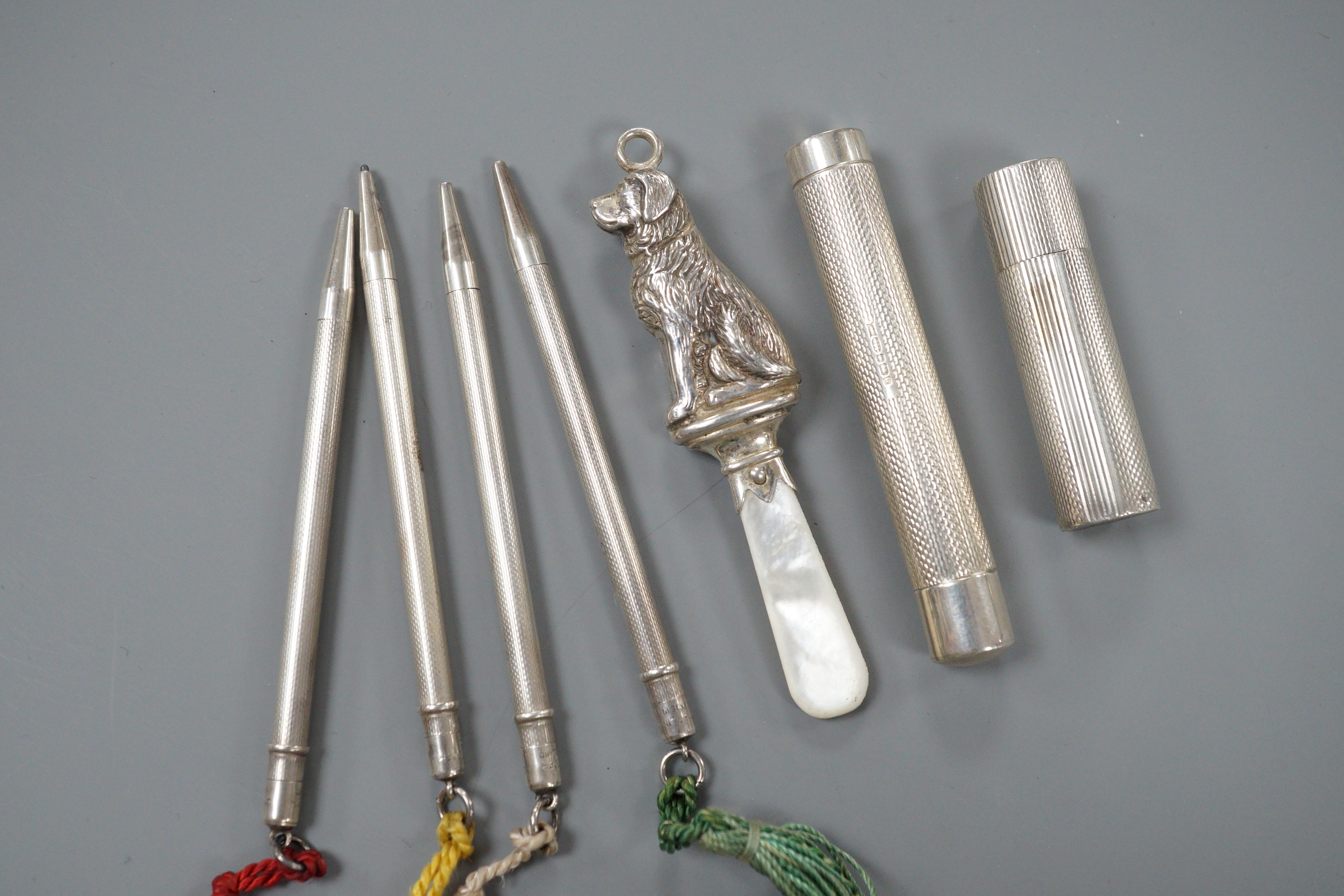 A 1950's engine turned silver lipstick holder, 5cm, a silver cylindrical case, a silver and mother of pearl 'dog' child's rattle and a set of four sterling pencils.